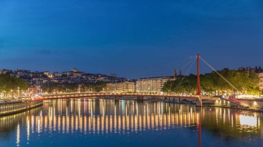 Lyon 'daki Saone Nehri' nin üzerindeki Palais du Justice Köprüsü 'nde, günden geceye geçiş. Rıhtımdaki aydınlık binalar gün batımından sonra suya yansıyor.