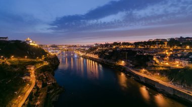 Day to night transition aerial view of the historic city of Porto, Portugal panoramic timelapse with the Dom Luiz bridge. Illuminated waterfront reflected in the river from above