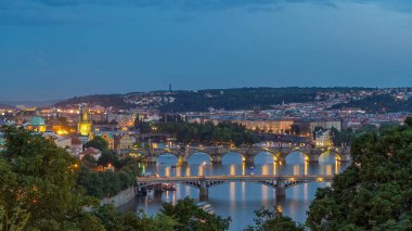 Vltava nehri üzerindeki köprülerin görüntüsü günden geceye geçiş zamanı ve Prag 'ın tarihi merkezi: kırmızı çatıları ve çok renkli duvarları olan eski kasabanın binaları ve simgeleri.
