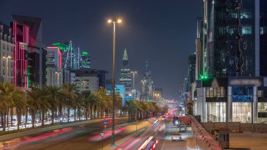 Riyad, Suudi Arabistan 'ın şehirsel gece zaman çizelgesinde aydınlık kuleler, cam gökdelenler, Kral Fahd Yolu ve yoğun trafik yer alıyor. Palmiyeler ve sokak lambaları şehrin içinden geçen ana otoyolda..