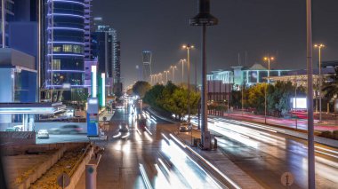 Suudi Arabistan 'ın Riyad kentindeki ikonik bükümlü gökdeleniyle King Fahd Yolu' ndaki yoğun karayolu trafiğinin hava takvimi görüntüsü. Dünyanın en yüksek sekizinci büküm kulesi. Aydınlatılmış sokaklar ve ağaçlar