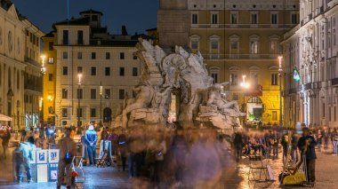 Four Rivers Zaman Kaynağı, Piazza Navona Roma, Fontana di Quattro Fiume, Bernini mermer heykeli. Arka planda turistler ve aydınlatılmış eski binalar