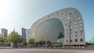Rotterdamse Markthal 'ın dış yüzeyinde aşırı kayma. Dükkanları ve restoranları olan ikonik at nalı şeklinde bir bina. Meydanda gezinen insanlar. Gökdelenler ve arka planda canlı bir şehir manzarası