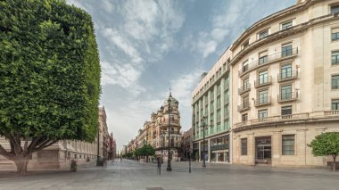 Avda boyunca yürüyen yayalar. De la Constitucion, Seville, İspanya 'nın Casco Antiguo bölgesindeki ana cadde. Edificio de la Adriatica ile zaman atlaması, tarihi binalar ve geçen tramvaylar
