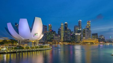 Futuristic architecture flower shape design of the Art Science museum day to night transition timelapse after sunset. Skyscrapers skyline city of Singapore.