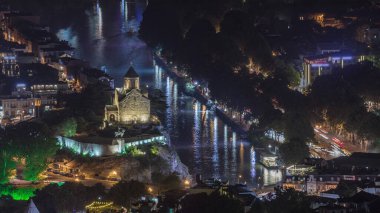 Metekhi Bakire Meryem Varsayımı Kilisesi 'nin hava gece zaman çizelgesi ve Kura Nehri üzerindeki Kral Vakhtang Gorgasali Heykeli. Köprüde trafik vardı ve rıhtım aydınlatılmıştı. Tiflis, Gürcistan.
