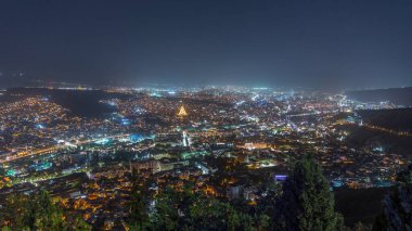 Tiflis şehir manzarası, Gürcistan günden geceye zaman. Şehir merkezinin ve Tiflis 'teki Kura Nehri' nin üst manzarası. Gökyüzünden Gürcistan başkentinin gökyüzü manzarası aydınlatılmış ünlü simgelerle