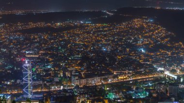 Gürcistan 'ın gökdelenleri, işlek bulvarda yer alan Tiflis hava zaman çizelgesinde aydınlatılmış cam kule. Tarihi bina ve nehir. Bakış açısından bak