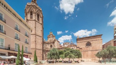 Valencia, İspanya 'da Plaza de la Reina' nın panoramik zaman atlaması. Tarihi bir kilise kulesi, hareketli kafeler ve sıcak Akdeniz mavi bulutlu gökyüzünün altında merkezi bir çeşme ile dolu canlı bir meydan..