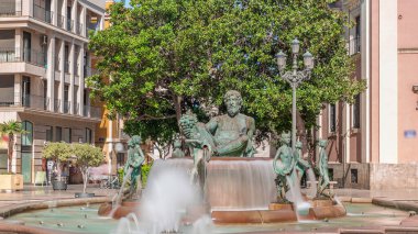 Valencia, İspanya 'daki ikonik Turia Pınarı ile birlikte Plaza de la Virgen' den Timelapse. Neptün heykeli Turia Nehri ve kanallarını temsil eder. İnsanlar yeşil ağaçlarla meydanda geziniyor.