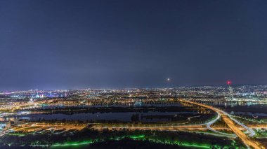 Viyana üzerinde gökdelenler, otoyol kavşağı, tarihi binalar ve Avusturya 'da nehir kenarında bir gece gezintisi olan panoramik manzara. Tuna Kulesi perspektifinden aydınlatılmış gökyüzü