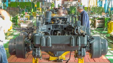 Konveyör montajı, traktörün gövdesini büyük endüstriyel fabrika zaman diliminde sahneleyecek. Çerçeve montajı, Chassis kurulumu ve diğer bölümler etrafındaki işçiler.