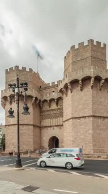 Serrans Kuleleri Torres de Serranos zaman atlaması. Valencia, İspanya 'da. Şehrin antik duvarlarından gelen büyük bir ortaçağ kapısı. Bulutlu bir gökyüzü altında hareketli bir sokak manzarası bu tarihi yeri çerçeveler.