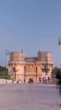 Serrans Kuleleri Torres de Serranos günden geceye Valencia, İspanya 'daki geçiş zamanı. Şehrin antik duvarlarından gelen büyük bir ortaçağ kapısı. İnsanlar tarihi bir yere yakın bir köprüde yürüyorlar.