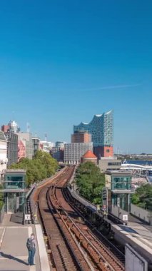 Almanya 'nın Hamburg kentindeki Landungsbrucken istasyonuna gelen trenler son sürat ilerliyor. Metroya binen insanlar mavi gökyüzünün altında Elbphilharmonie, liman ve marina ile panoramik manzara