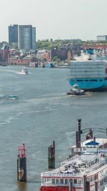 Almanya 'nın Hamburg kentinde Elbe nehir kenarının hava zaman çizelgesi. İskeleye yakın tekneler, Jan Fedder gezinti güvertesi, marina ve konteyner gemilerinin geçtiği manzara. Elbe Nehri kıyısındaki canlı şehir manzarası