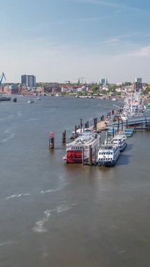 Almanya 'nın Hamburg kentinde Elbe nehir kenarının hava zaman çizelgesi. Rıhtımın yakınındaki Jan Fedder Gezinti Güvertesi, marina ve geçen gemilerle sahile manzara. Elbe Nehri kıyısındaki canlı şehir manzarası