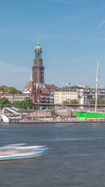 Elbe nehir kenarı ve Hamburg, Almanya 'daki St. Michaels kilise kulesinin panoramik zaman çizelgesi. İskeleye yakın teknelerle manzara, Jan Fedder gezinti güvertesi ve oradan geçen feribotlar. Nehir kenarındaki canlı şehir manzarası