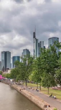 Almanya 'nın Frankfurt kentindeki ana nehir üzerindeki tarihi Eiserner Steg Demir Köprüsü' nün hızlandırılması. Gökdelenler ufuk çizgisi ve kıyı şeridi bulutlarla dolu bir gökyüzünün altında yansıyor.