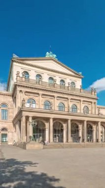 Hanover Devlet Operası Staatsoper Hannover ön görüntüsü. Şehir meydanında canlı mavi bulutlu bir zaman dilimi altında yürüyen insanların olduğu klasik tarzda bir tiyatro. Almanya