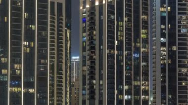 Şehrin hava zaman ayarlı yerleşim bölgesinde parlayan pencereleri olan uzun apartmanlar. Kulelerdeki dairelerin odalarında akşam ışığı ve aydınlatılmış gökdelenler