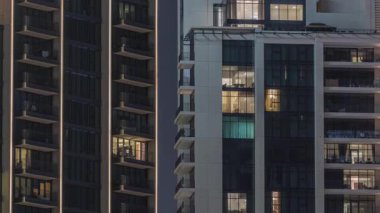 Şehrin hava zaman ayarlı yerleşim bölgesinde parlayan pencereleri olan uzun apartmanlar. Gökdelenlerdeki ve kulelerdeki dairelerde akşam ışığı