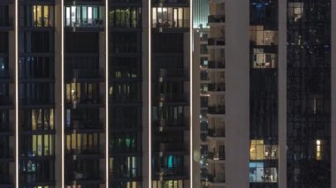 Şehrin hava zaman ayarlı yerleşim bölgesinde parlayan pencereleri olan uzun apartmanlar. Kulelerdeki ve gökdelenlerdeki odalarda akşam sarı ışığı