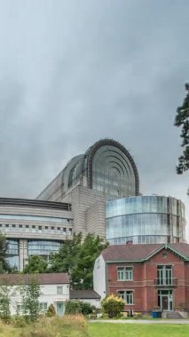 Brüksel 'deki Avrupa Mahallesi' ndeki binalar Avrupa Parlamentosu, Komisyon ve dramatik bulutlu gökyüzü altındaki kurumlarla aynı tarihe denk geliyor. Leopold Park ön planda kırmızı tuğlalı evle