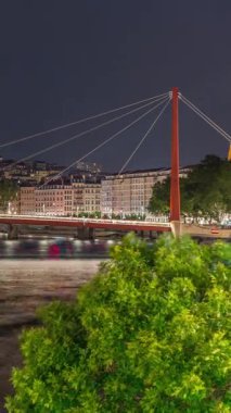 Saone Nehri üzerindeki kırmızı asma köprü ile Lyons şehir manzarasının gece zaman çizelgesi, aydınlatılmış kıyı şeridi gece boyunca suya yansıdı. Fransa