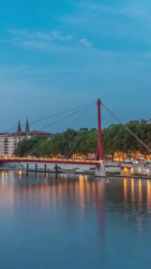 Lyon 'daki Saone Nehri' nin üzerindeki Palais du Justice Köprüsü 'nde, günden geceye geçiş. Rıhtımdaki aydınlık binalar gün batımından sonra suya yansıyor.
