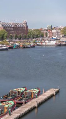 Oosterdok Limanı 'ndaki iskelede botları olan Amsterdam gökyüzü manzarası. Amsterdam Centraal İstasyonu ve Scheepvaarthuis yakınlarındaki geleneksel Hollanda mimarisi. Amsterdam, Hollanda