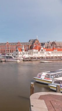 Amsterdam Merkez Tren İstasyonu 'nun zaman çizelgesi. Rıhtımda demirlemiş tur botları, geçen tramvaylar ve ön planda bir kanal var. Amsterdam, Hollanda