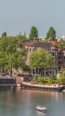 Amsterdam şehri, Montelbaanstoren Kulesi 'nin yer aldığı, kanal boyunca uzanan şehir manzaralı bir zaman çizelgesi. Eski kentteki tarihi Hollanda evleri, köprüler, mavnalar ve yüzen evler