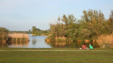 İki genç bayan, Hollanda, Amsterdam 'daki Gaasperdammer Plas' ta çimlerin üzerinde güneşin tadını çıkarıyorlar.