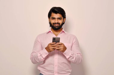 Yakışıklı, sakallı, resmi tişört giyen, akıllı telefon tutan ve iş arkadaşlarıyla mesajlaşan, mutlu gülümseyen, kendinden emin bir iş adamı.