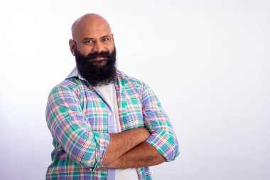 Hintli güçlü, sağlıklı, kendine güveni tam kel, ayakta duran ve kollarını kavuşturup kameraya bakan adam.