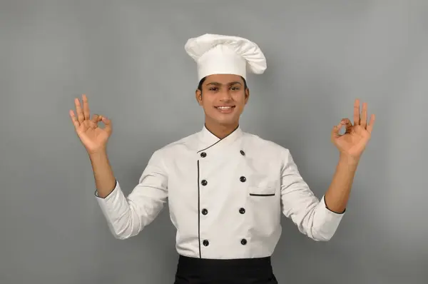 Happy male Indian chef showing ok gesture with one hand over grey background, profession and people concept