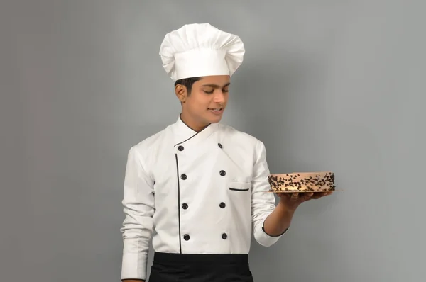 Happy male Indian chef Confectioner decorating chocolate cake, doing icing on the cake