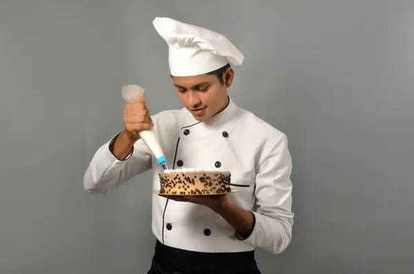 Happy male Indian chef Confectioner decorating chocolate cake, doing icing on the cake
