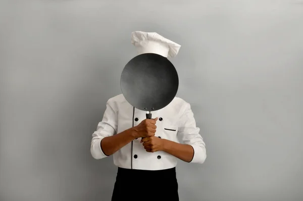 Confident smiling successful Indian chef holding a frying pan and pointing, profession and people concept