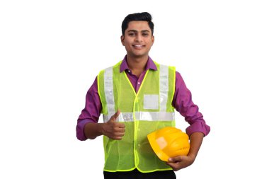 Güvenlik ceketi giymiş gülümseyen Hintli erkek mimar stüdyoda baş parmağını kaldırıyor..