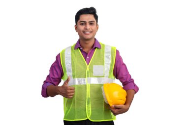 Güvenlik ceketi giymiş gülümseyen Hintli erkek mimar stüdyoda baş parmağını kaldırıyor..