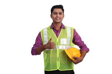 Güvenlik ceketi giymiş gülümseyen Hintli erkek mimar stüdyoda baş parmağını kaldırıyor..