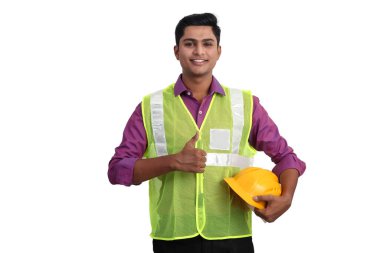 Güvenlik ceketi giymiş gülümseyen Hintli erkek mimar stüdyoda baş parmağını kaldırıyor..