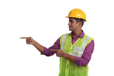 Sarı kask ve güvenlik ceketi giyen Hintli erkek mimar beyaz arka planı işaret ediyor.