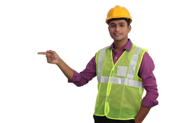 Sarı kask ve güvenlik ceketi giyen Hintli erkek mimar beyaz arka planı işaret ediyor.