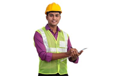 Hintli erkek mimar sarı kask ve güvenlik ceketi giyiyor. Stüdyoda dururken pano kullanarak bir şeyler yazıyor.