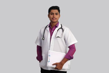 Boynunda steteskop olan genç, yakışıklı Hintli erkek doktor, beyaz arka planda izole bir klasör tutuyor. 