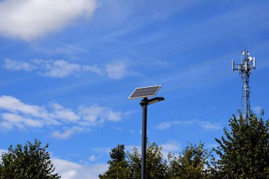 Güneş panelleri olan modern manzara fenerleri, ağaçların ve mavi gökyüzünün arka planına karşı baz istasyonu