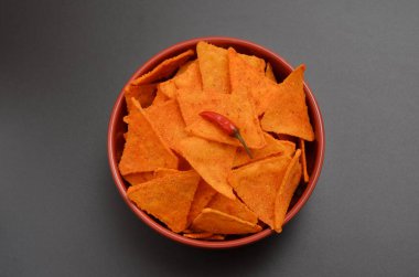 bowl with spicy mexican chips and chili peppers on a dark background, flat lay
